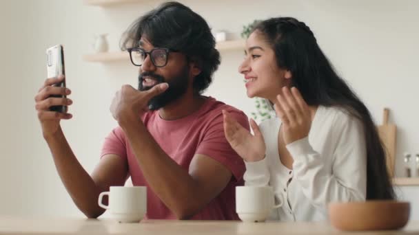Πολυφυλετική Ινδή αραβίδα γυναίκα κορίτσι και ο άνθρωπος τύπος μιλάμε κινητό τηλέφωνο στο σπίτι κουζίνα ποικίλο ζευγάρι κουβεντιάζοντας με τους φίλους σε απευθείας σύνδεση βίντεο κλήση μακρινή συνάντηση χαμογελαστοί σύζυγοι επικοινωνούν με το κινητό τηλέφωνο - Πλάνα, βίντεο