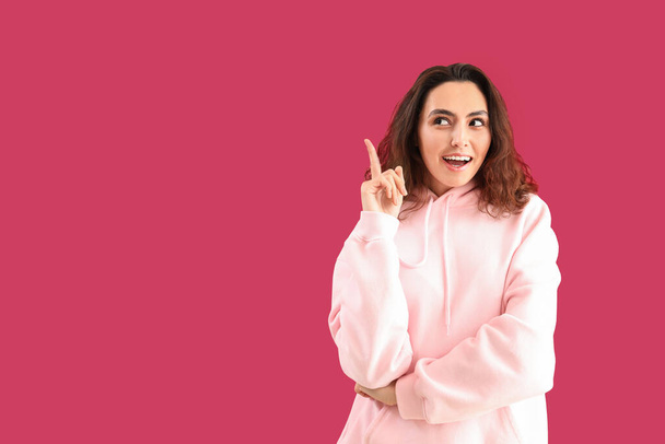 jonge vrouw in hoodie wijzend op iets op roze achtergrond - Foto, afbeelding