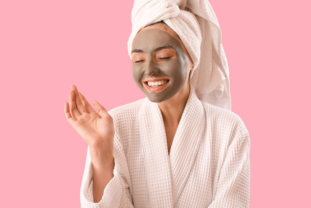 Young woman in bathrobe with applied clay mask on pink background - Φωτογραφία, εικόνα