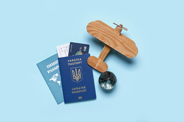 Ukrainian and immune passports with wooden airplane on blue background - Photo, Image