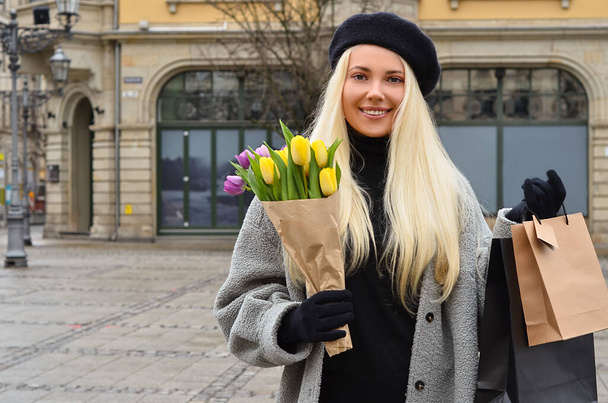Mujer joven con ramo de tulipanes y bolsas de compras en la calle de la ciudad - Foto, Imagen