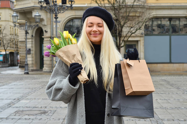 Young woman with bouquet of tulips and shopping bags on city street - Photo, Image