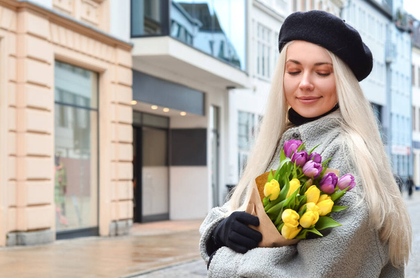 Молодая женщина с букетом тюльпанов на городской улице - Фото, изображение