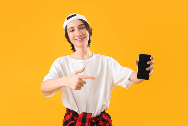 Cool tiener jongen wijzen naar mobiele telefoon op gele achtergrond - Foto, afbeelding