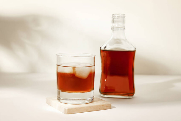 Μπουκάλι και ποτήρι κρύο ρούμι σε μπεζ φόντο - Φωτογραφία, εικόνα