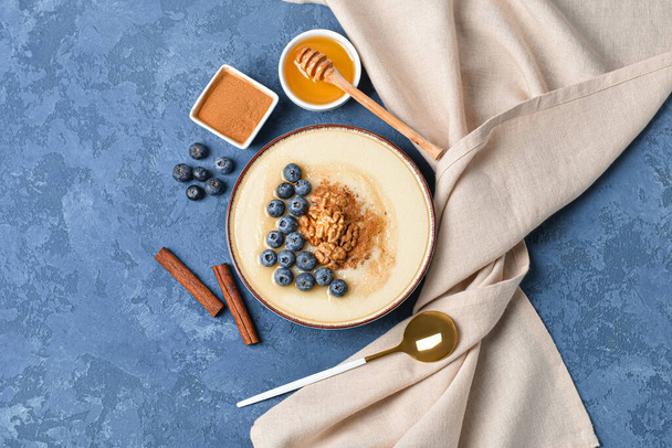 Schaal van smakelijke griesmeel pap met bosbes, kaneel, noten en honing op kleur achtergrond - Foto, afbeelding
