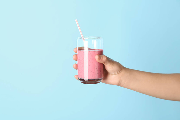 Female hand with glass of pink smoothie on blue background - Photo, Image