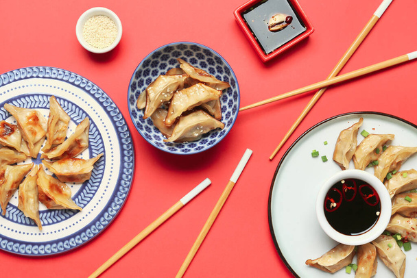 Тарелки с вкусным китайским цзяоцзы и соусом на красном фоне - Фото, изображение