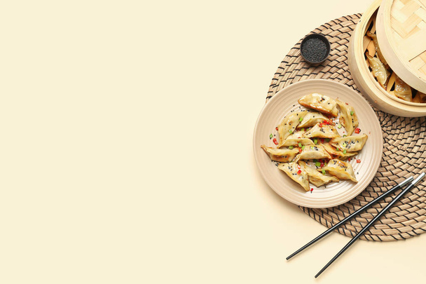 Placa com saboroso jiaozi chinês, gergelim e vapor de bambu no fundo bege - Foto, Imagem