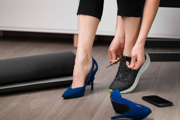 Kobieta zmienia wysokie obcasy na sportowe buty do biegania. Ćwiczenia pozalekcyjne, koncepcja zdrowego stylu życia. - Zdjęcie, obraz
