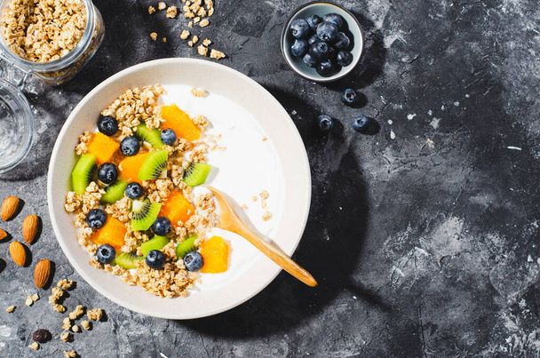 Yogurt with Granola, Kiwi, Blueberries, and Orange in a Bowl, Healthy Snack or Breakfast on Dark Background - Fotó, kép