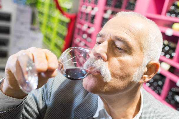smiling senior man tatsing wine at the supermarket - Фото, изображение