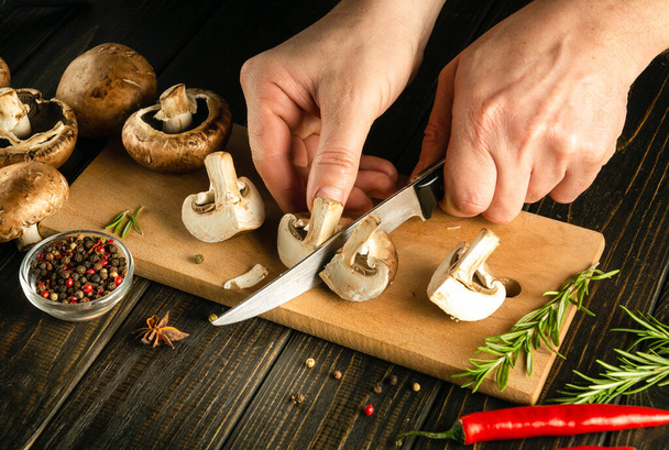 Une idée de régime aux champignons. Cuisson des champignons Agaricus par les mains du chef dans la cuisine. Espace sombre pour la recette ou le menu - Photo, image