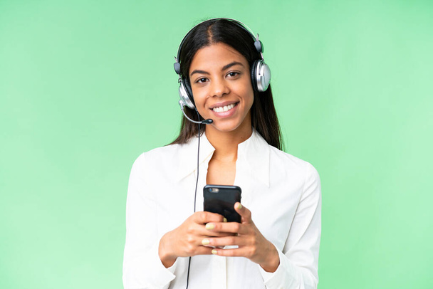 Telemarketer African American woman working with a headset over isolated chroma key background sending a message with the mobile - 写真・画像