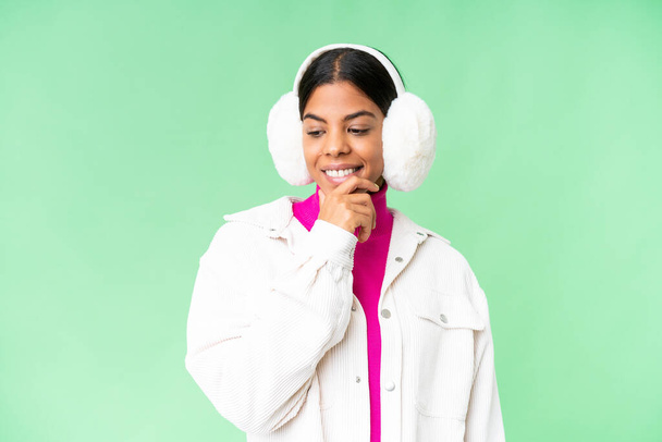Молода афроамериканка носить зимові муфти через ізольований хроматичний фон, що дивиться збоку. - Фото, зображення