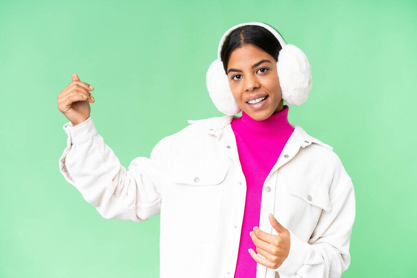 Young African American woman wearing winter muffs over isolated chroma key background making guitar gesture - Foto, Imagen