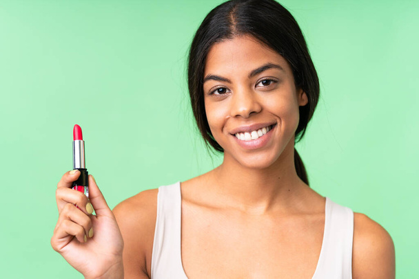 Young woman over over isolated chroma key background holding red lipstick - Foto, Imagem