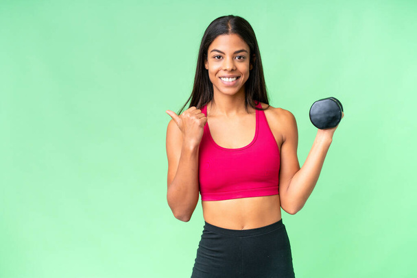 若いアフリカ系アメリカ人女性のスポーツ女性は、製品を提示する側を指して隔離されたクロマキーの背景に重量挙げを行う - 写真・画像