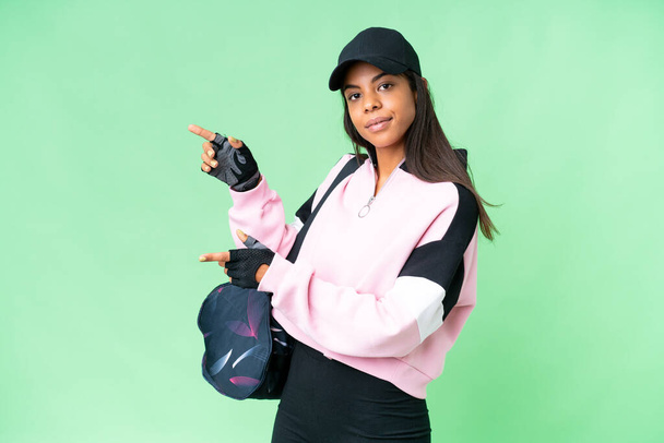 Молода афроамериканська жінка зі спортивним пакетом через ізольований хроматичний ключ вказує пальцем збоку і представляє продукт - Фото, зображення