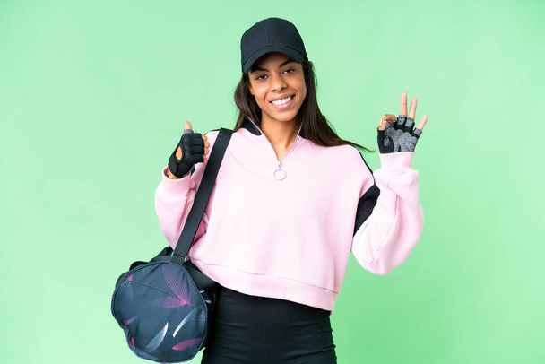 Νεαρή σπορ Αφρο-Αμερικανίδα γυναίκα με τσάντα αθλητισμού πάνω από απομονωμένο φόντο chroma κλειδί δείχνει ok σημάδι και τον αντίχειρα μέχρι χειρονομία - Φωτογραφία, εικόνα