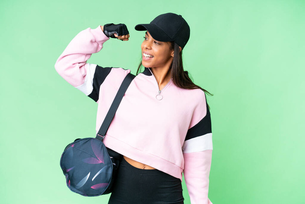 Νεαρή άθλημα Αφρο-αμερικανική γυναίκα με τσάντα αθλητισμού πάνω από απομονωμένο φόντο chroma κλειδί κάνει ισχυρή χειρονομία - Φωτογραφία, εικόνα