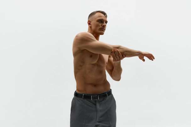 Muskelkräftiger Körper in Bewegung. Aufnahme eines attraktiven Mannes in Hose, der ohne Hemd dasteht und vor weißem Hintergrund vor der Kamera posiert. Konzept der Männermode, Stil, Körperästhetik, Schönheit, Männergesundheit - Foto, Bild