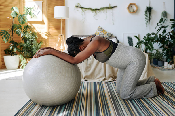 African pregnant woman standing on knees leaning on fitness ball feeling pain during contractions, she giving birth at home - Photo, Image