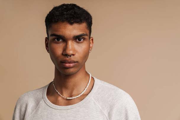 Portrait of young handsome serious african man looking at camera , while standing over isolated beige background - Valokuva, kuva