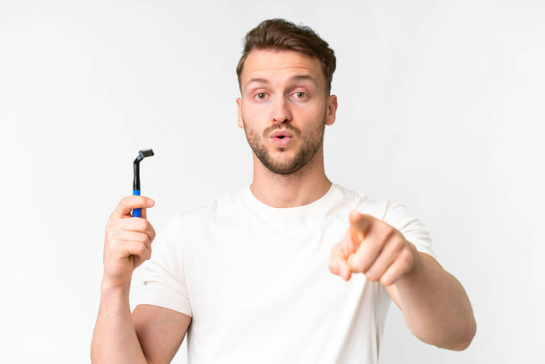 jovem caucasiano homem barbear sua barba sobre isolado branco fundo surpreso e apontando frente - Foto, Imagem