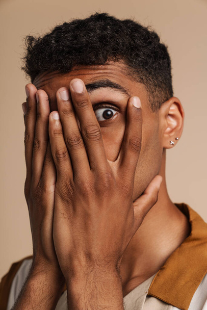 Shocked black man covering his face and looking at camera isolated over beige background - Foto, afbeelding