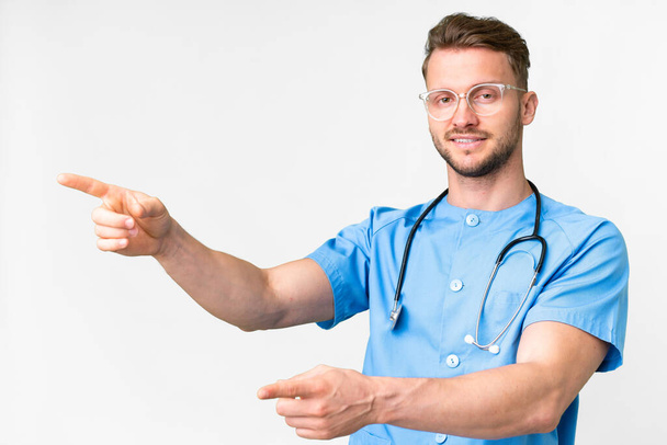 Young nurse man over isolated white background pointing finger to the side and presenting a product - Fotografie, Obrázek