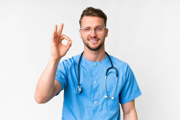 Young nurse man over isolated white background showing ok sign with fingers - Foto, imagen