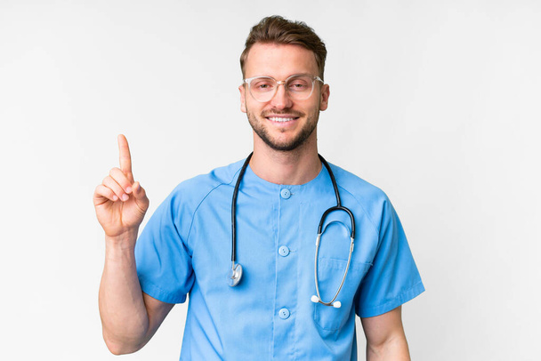 Young nurse man over isolated white background showing and lifting a finger in sign of the best - Foto, immagini