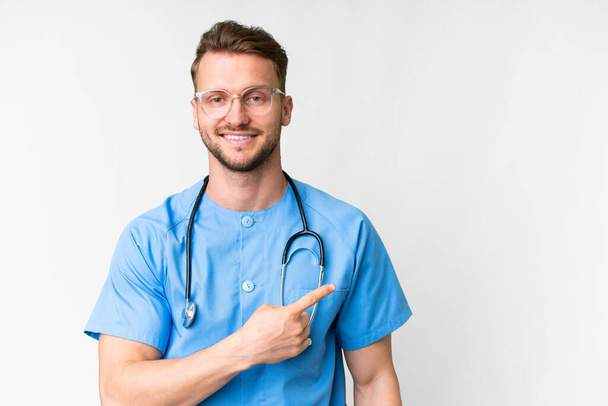 Jonge verpleegkundige man over geïsoleerde witte achtergrond wijzend naar de zijkant om een product te presenteren - Foto, afbeelding