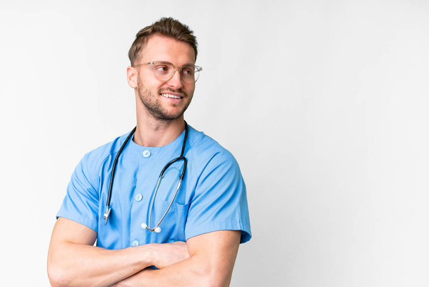 Young nurse man over isolated white background with arms crossed and happy - Фото, изображение