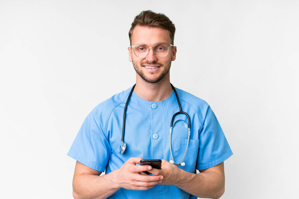 Young nurse man over isolated white background sending a message with the mobile - 写真・画像