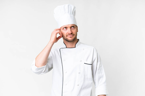 Młody kucharz kaukaski na białym tle z wątpliwościami i zdezorientowanym wyrazem twarzy - Zdjęcie, obraz