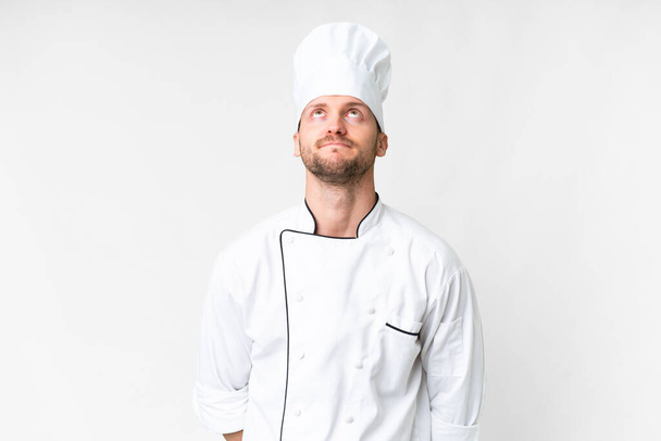 Молодий кавказький шеф-кухар над ізольованим білим тлом і дивиться вгору
 - Фото, зображення