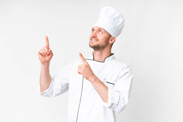 Jonge Kaukasische chef-kok over geïsoleerde witte achtergrond wijzen met de wijsvinger een geweldig idee - Foto, afbeelding