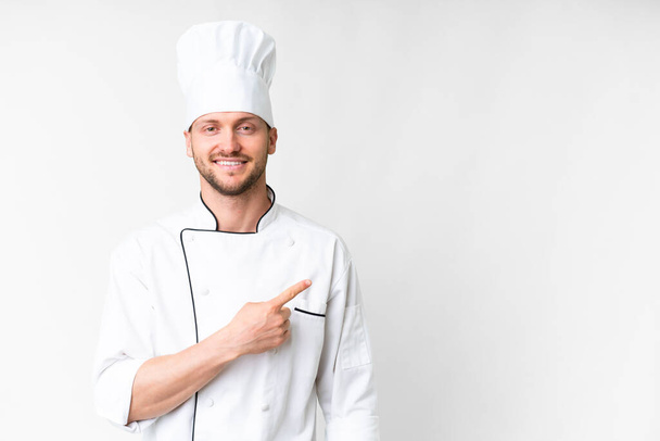 Giovane chef caucasico su sfondo bianco isolato che punta verso il lato per presentare un prodotto - Foto, immagini