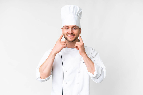 młody kaukaski kucharz nad odizolowanym białym tle uśmiecha się z szczęśliwy i przyjemny wyraz - Zdjęcie, obraz