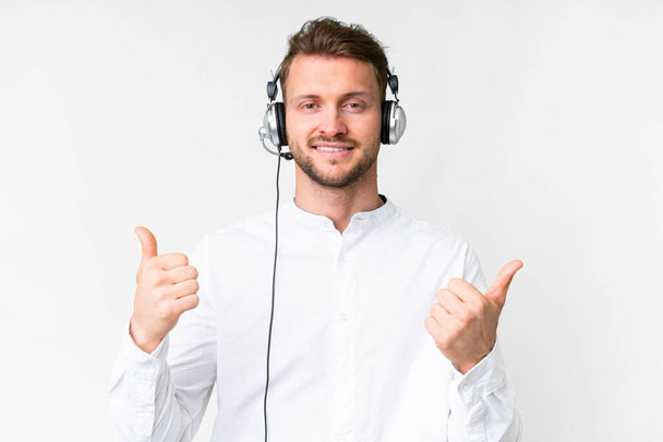 Telemarketer hombre caucásico trabajando con un auricular sobre fondo blanco aislado con los pulgares hacia arriba gesto y sonriendo - Foto, Imagen