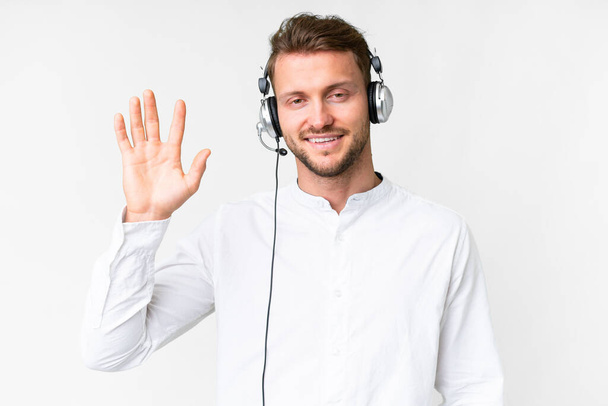 Hombre caucásico telemarketer trabajando con un auricular sobre fondo blanco aislado saludando con la mano con expresión feliz - Foto, Imagen