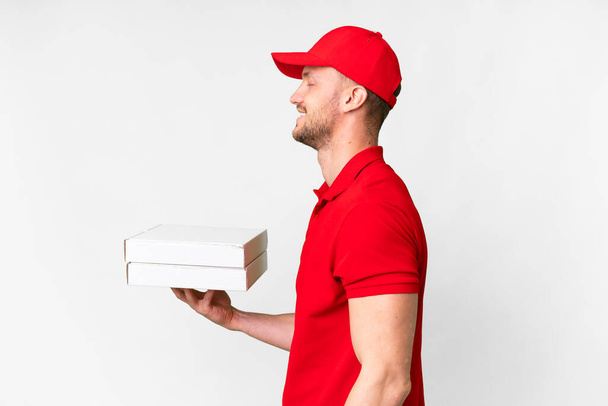 Repartidor de pizza con uniforme de trabajo recogiendo cajas de pizza sobre fondo blanco aislado riendo en posición lateral - Foto, Imagen