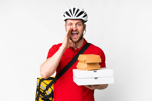 Young delivery man taking a takeaway food over isolated white background shouting with mouth wide open - Photo, Image