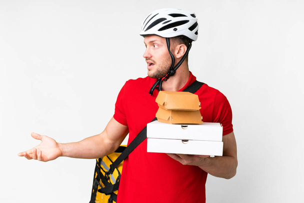 Young delivery man taking a takeaway food over isolated white background with surprise expression while looking side - Foto, immagini