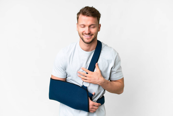 Young caucasian man with broken arm and wearing a sling over isolated white background smiling a lot - Foto, immagini