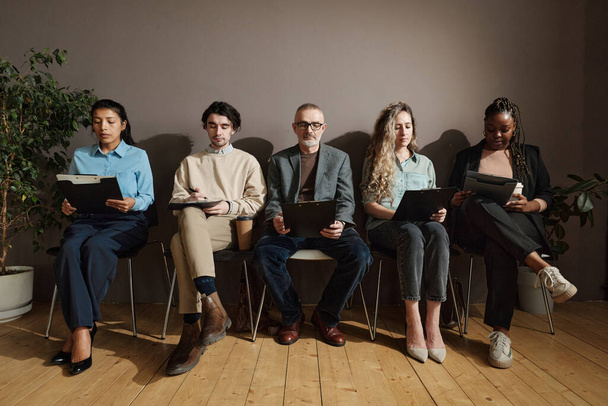 Grupo de empresarios sentados en sillas en la sala de espera y leyendo contrato antes de conseguir un trabajo - Foto, imagen
