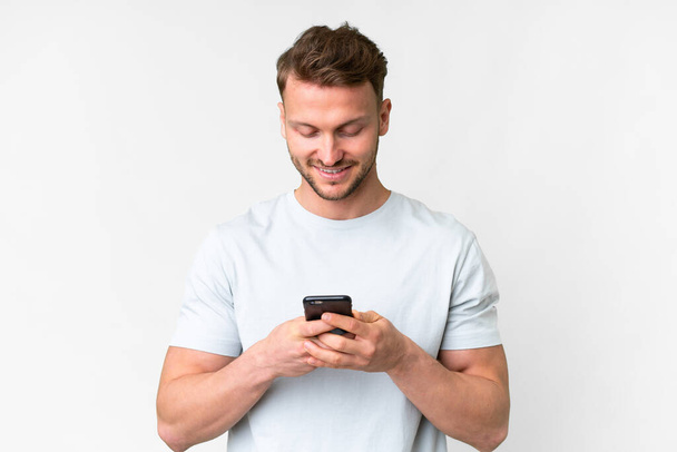 Jovem caucasiano bonito sobre fundo branco isolado enviando uma mensagem ou e-mail com o celular - Foto, Imagem