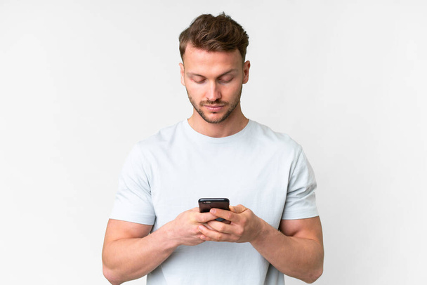 Молодой красивый белый мужчина на изолированном белом фоне с помощью мобильного телефона - Фото, изображение